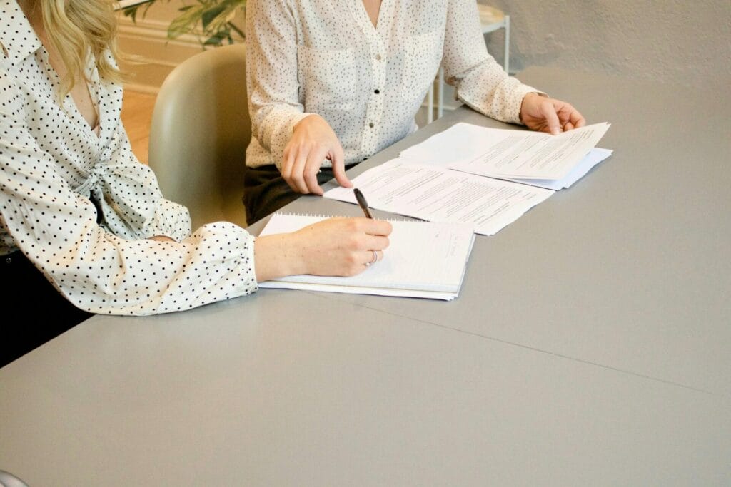 Two employees at a desk review paperwork together.